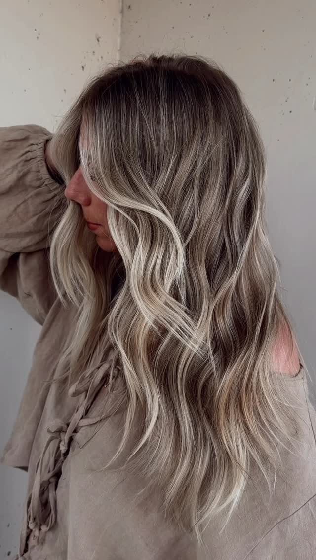 Woman with long wavy ash-blonde hair and softly blended dark roots