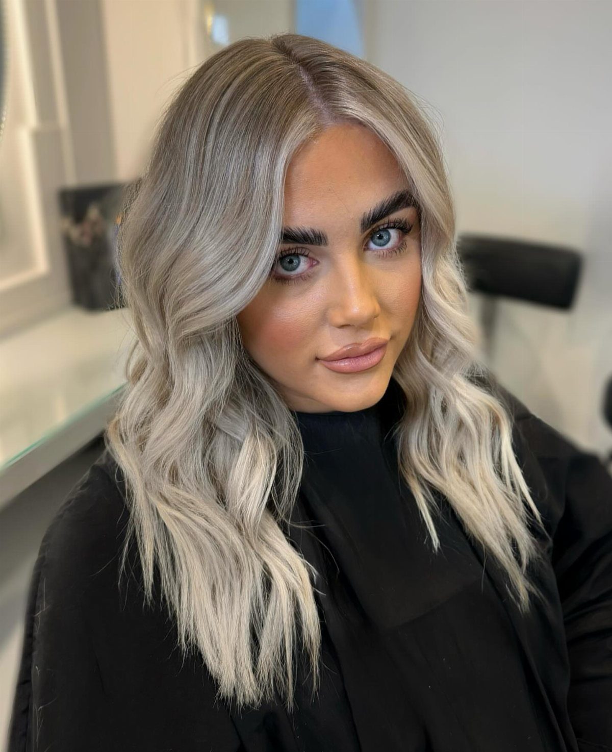 Woman with cool bronde waves, dark roots, and bright silver face-framing highlights