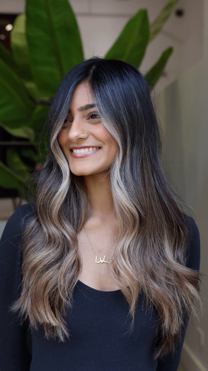 Woman with long dark waves and face-framing ash-blonde balayage