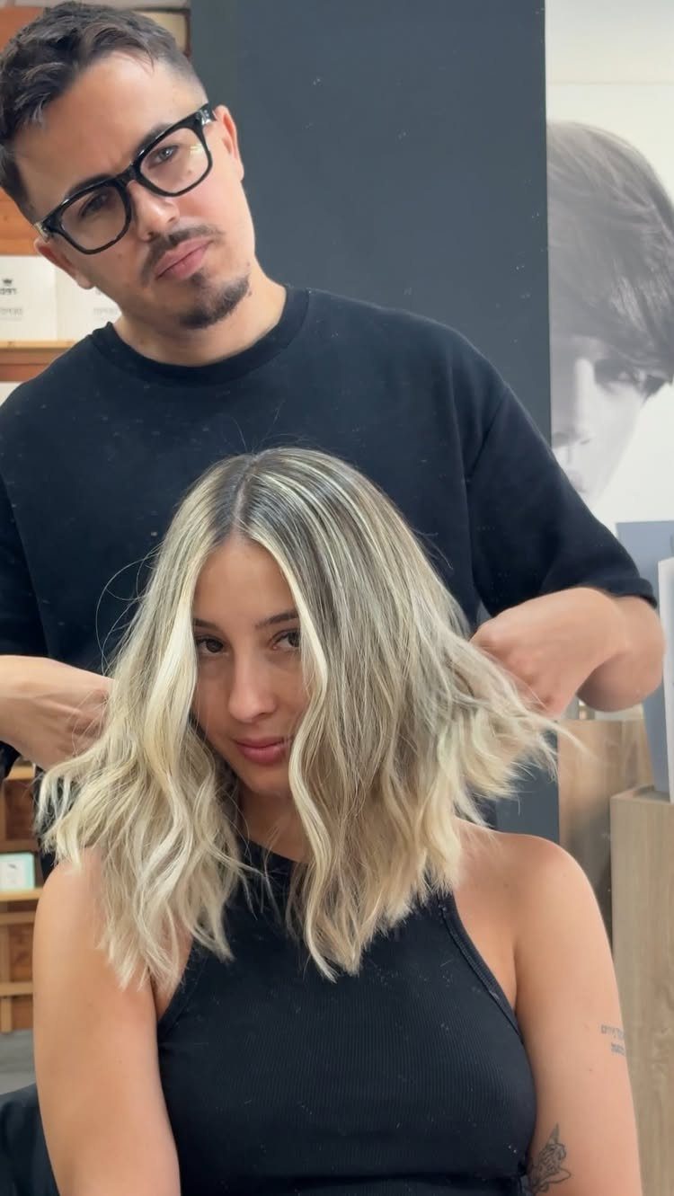 Woman with a dark-rooted, wavy light ash-blonde lob in a salon