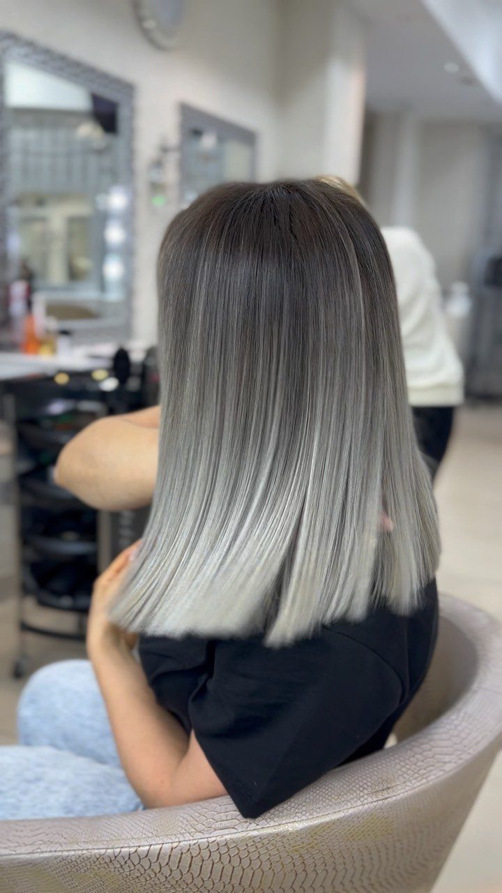 Long straight hair with dark roots and cool ash-blonde babylights in a salon