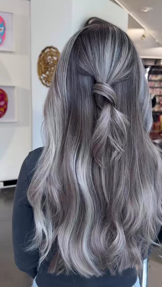 Long smoky silver-gray hair falls in waves with dark roots and a half-up twist.