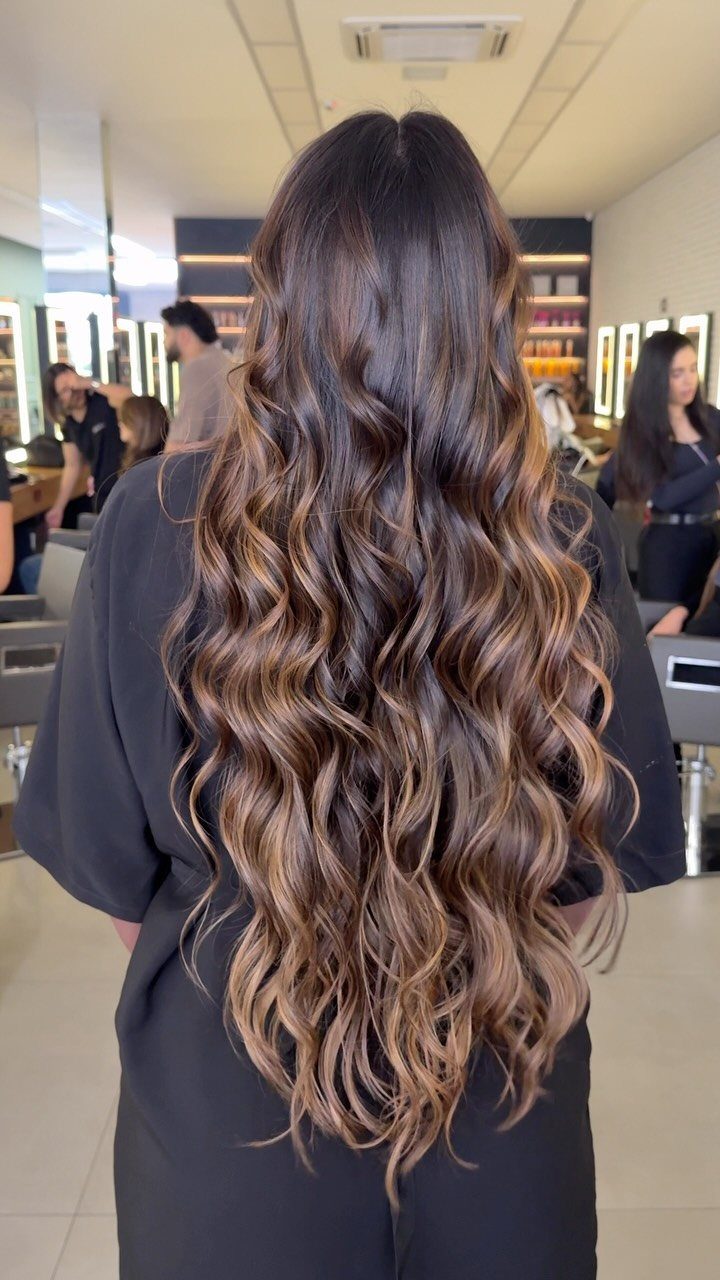 Long wavy chocolate-brown hair with softly blended toffee highlights in a salon