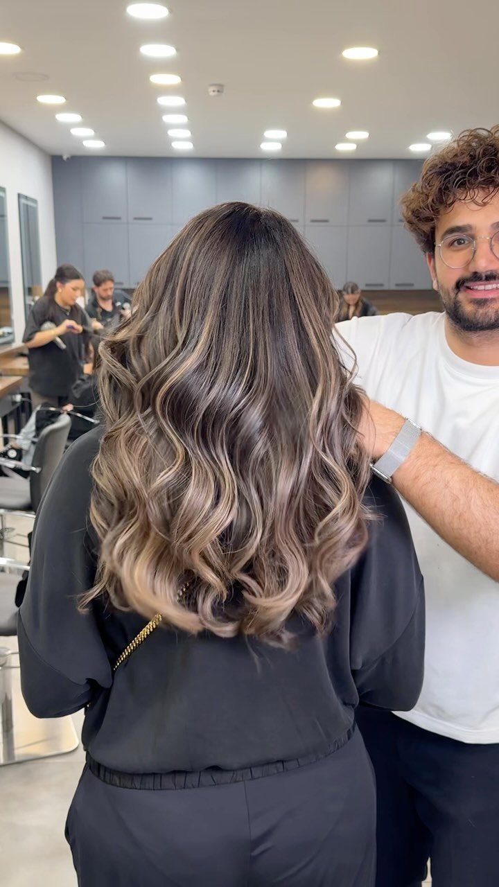 Long wavy dark brown hair with blended blonde balayage highlights in a salon