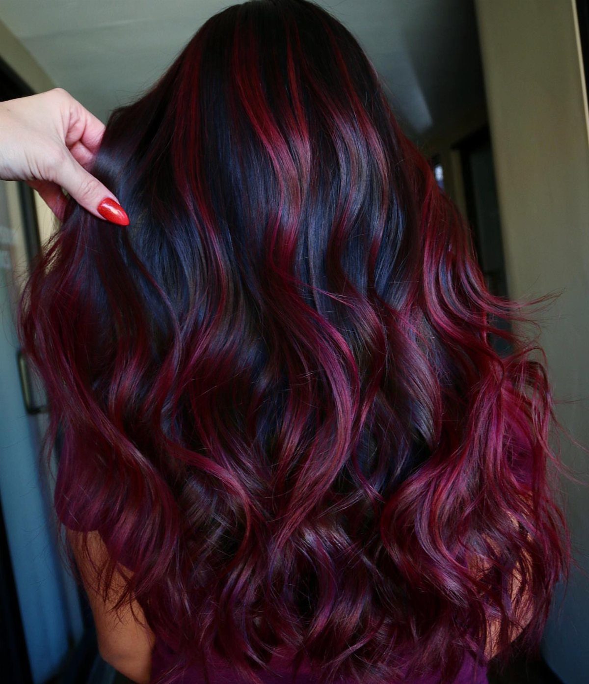 Wavy dark hair with vivid burgundy-red ribbons and a hand touching it