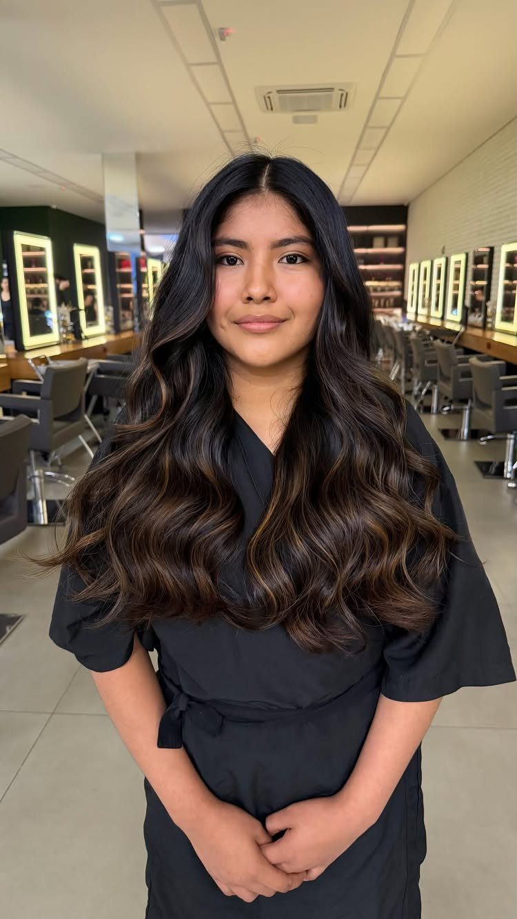 Woman displaying long dark waves with subtle hazelnut-brown highlights in a salon