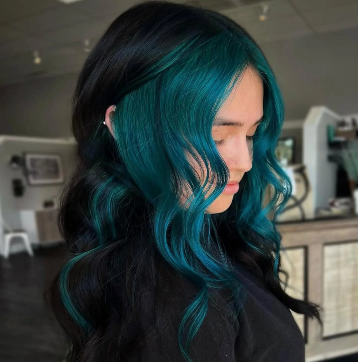 Dark wavy hair with vivid teal highlights shown in a salon