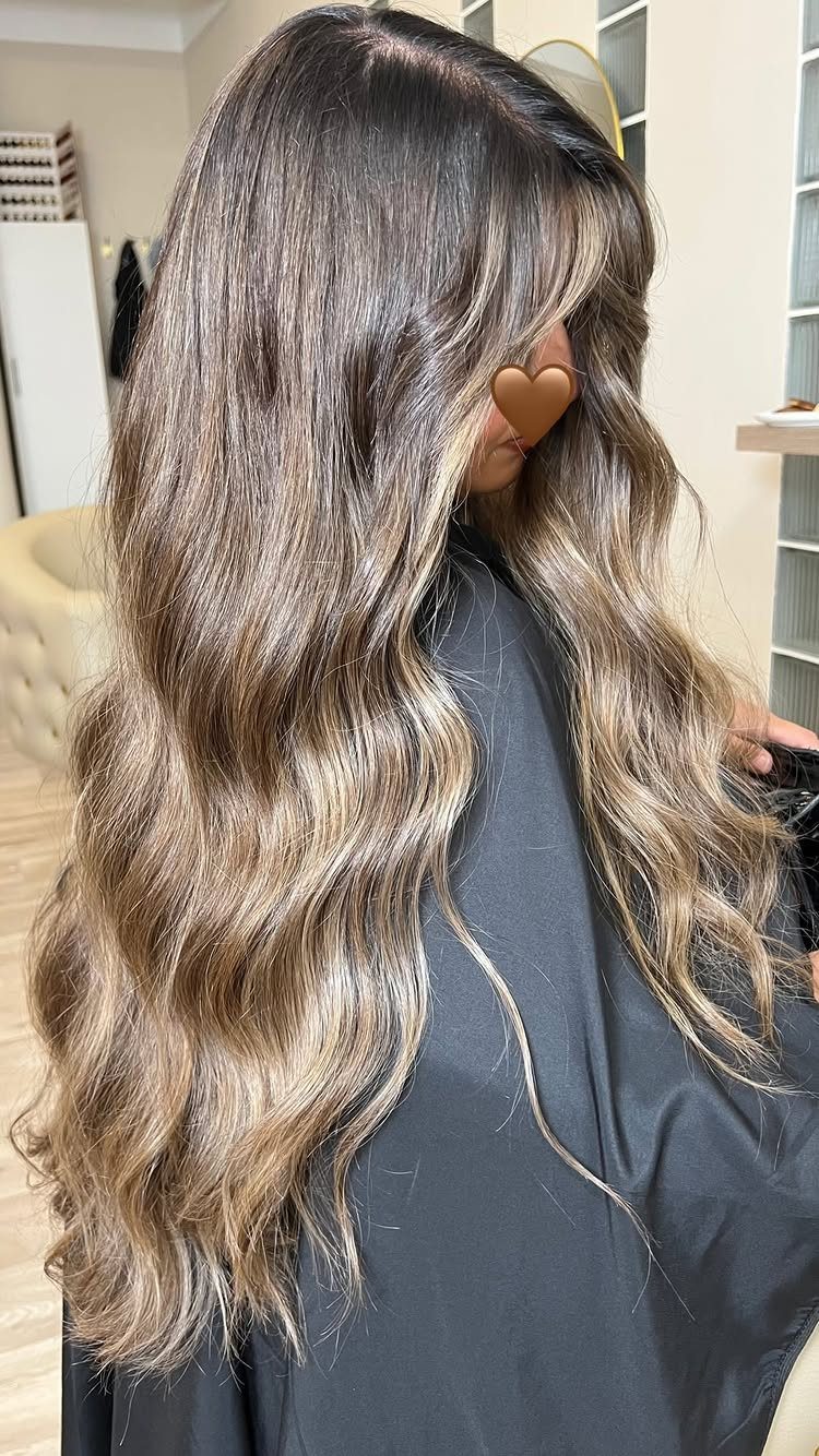 Wavy dark-rooted hair blends into dimensional beige blonde lengths in a salon