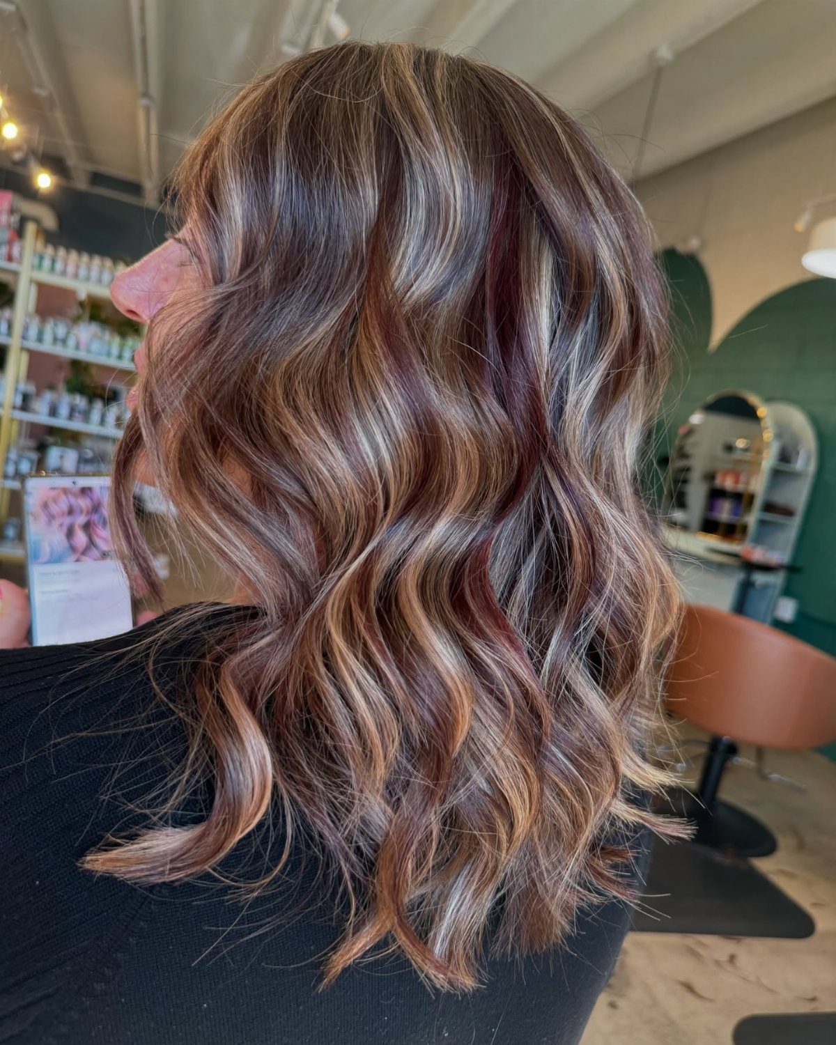 Wavy shoulder-length hair with burgundy, copper, and blonde highlights in a salon