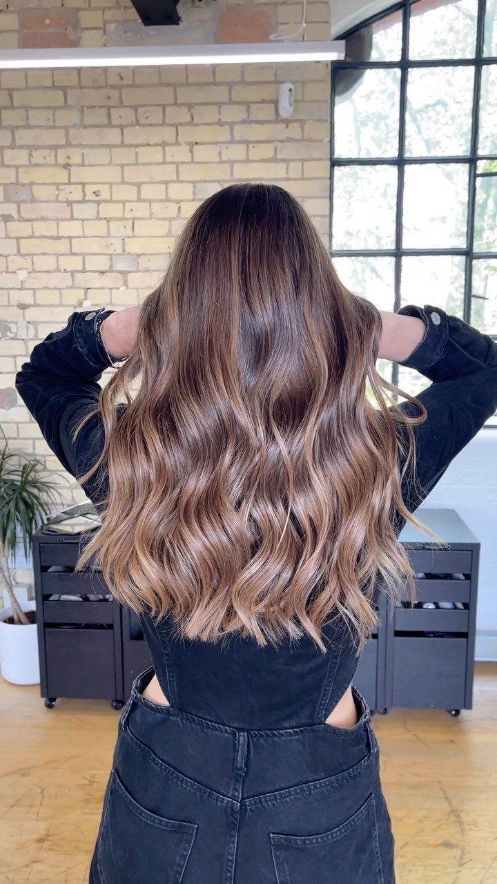 Long wavy brown hair with warm caramel-blonde balayage highlights and lighter ends