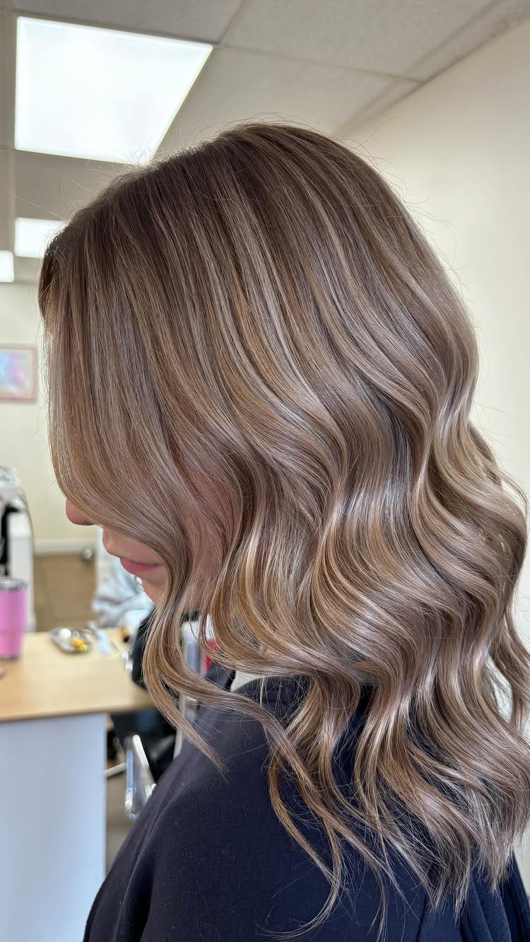 Long dark dirty blonde hair with subtle balayage and loose waves in a salon