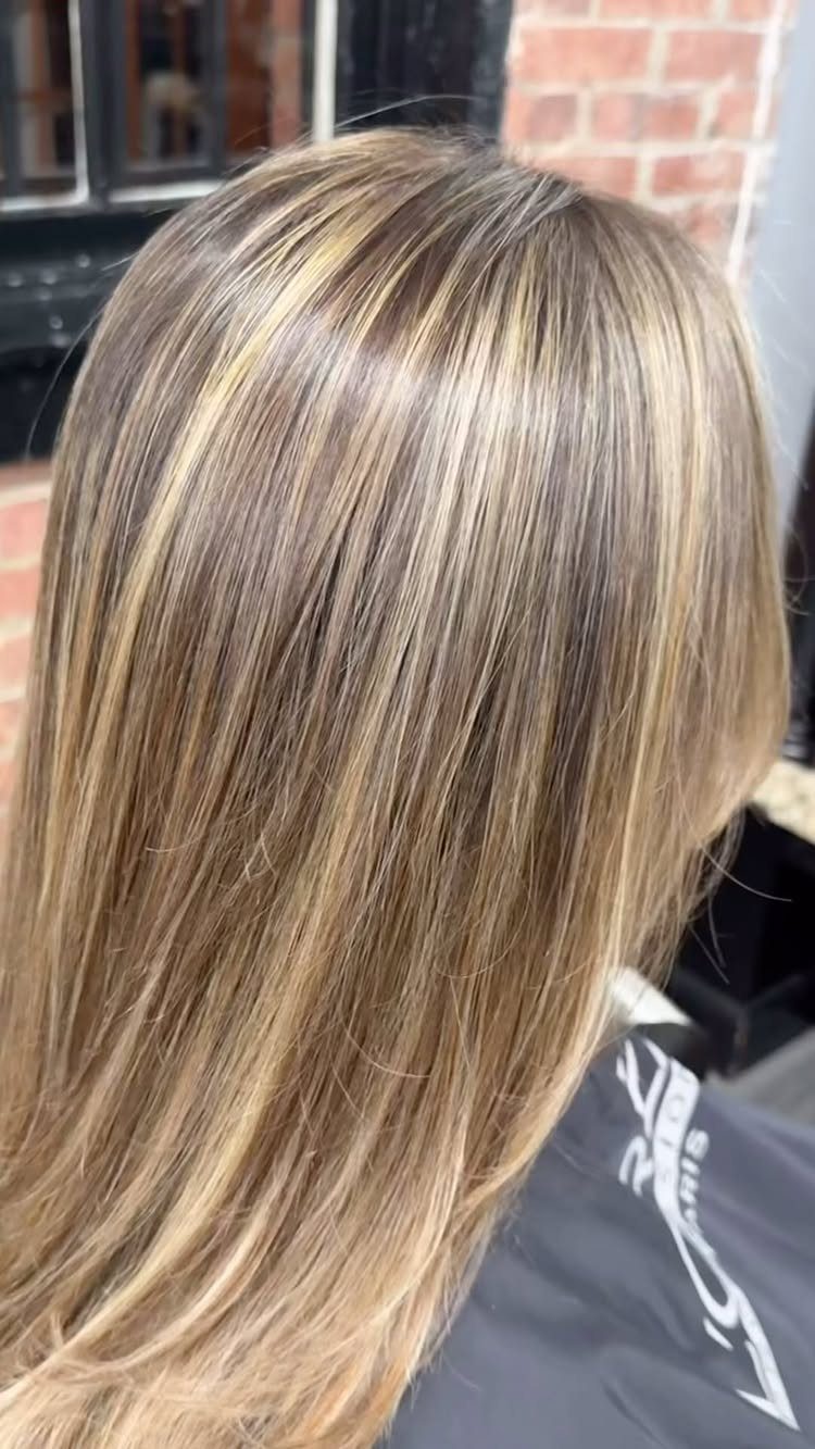 Long blonde hair with fine golden highlights drapes over a black salon cape