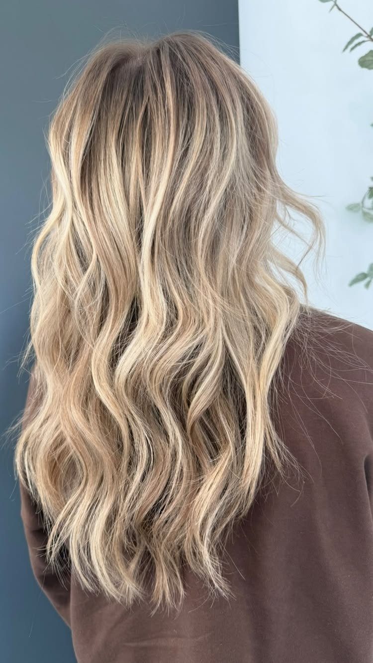 Long wavy blonde hair with darker lowlights over a dark brown top