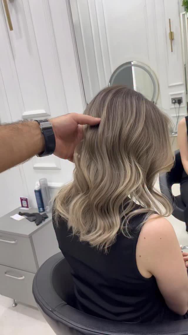 Wavy dishwater blonde hair with darker roots seen from behind in a salon