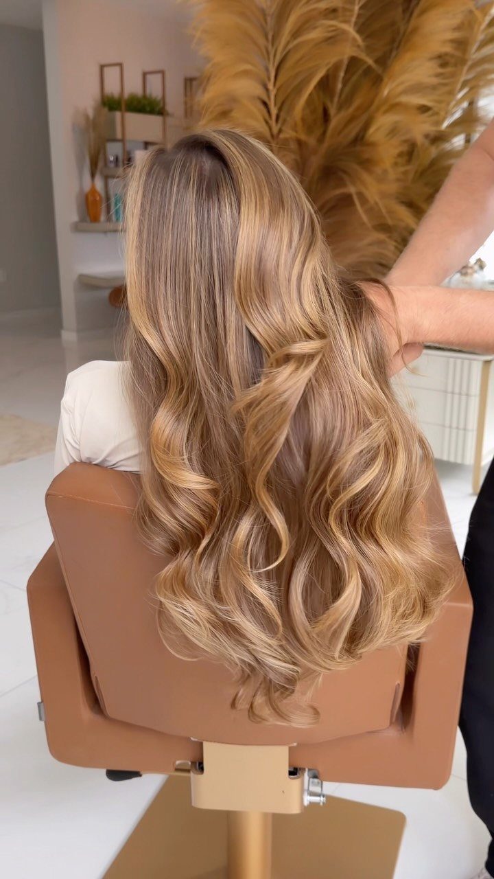 Long wavy blonde hair with dark roots and warm honey-golden balayage