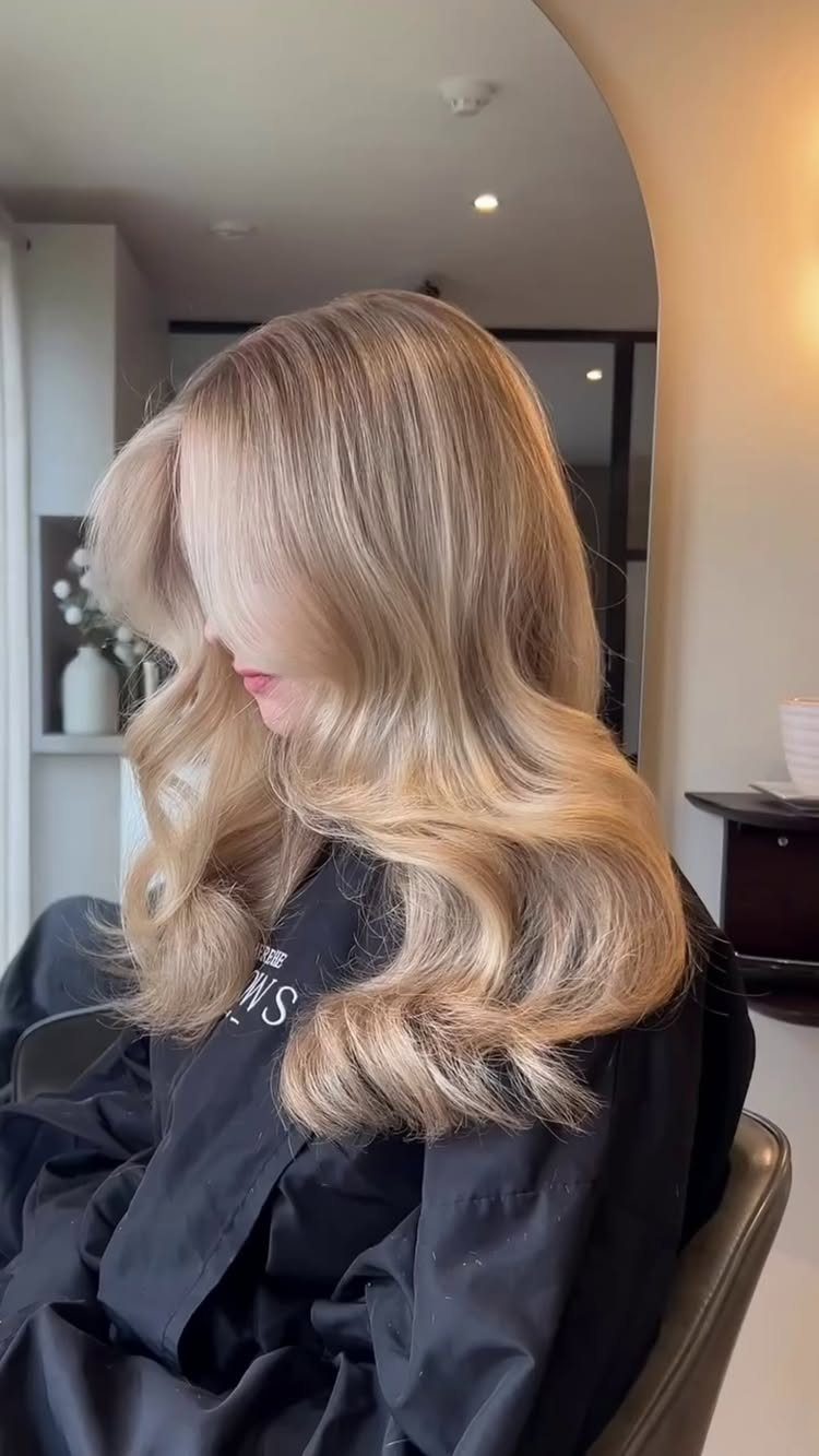 Long blonde balayage with darker roots and softly curled, blended ends