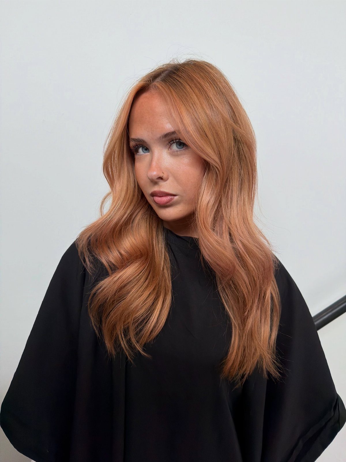 Woman with long, wavy strawberry-blonde balayage wearing a black salon cape