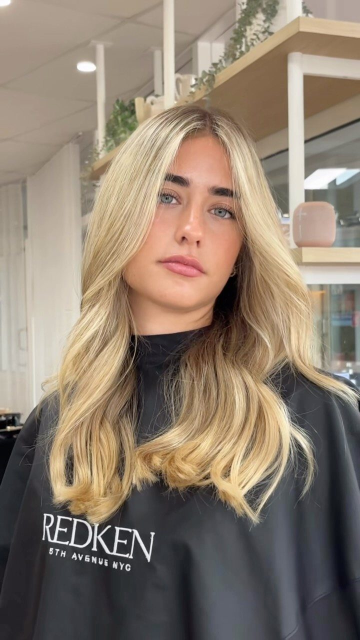 Woman with long, wavy blonde balayage hair wearing a black salon cape