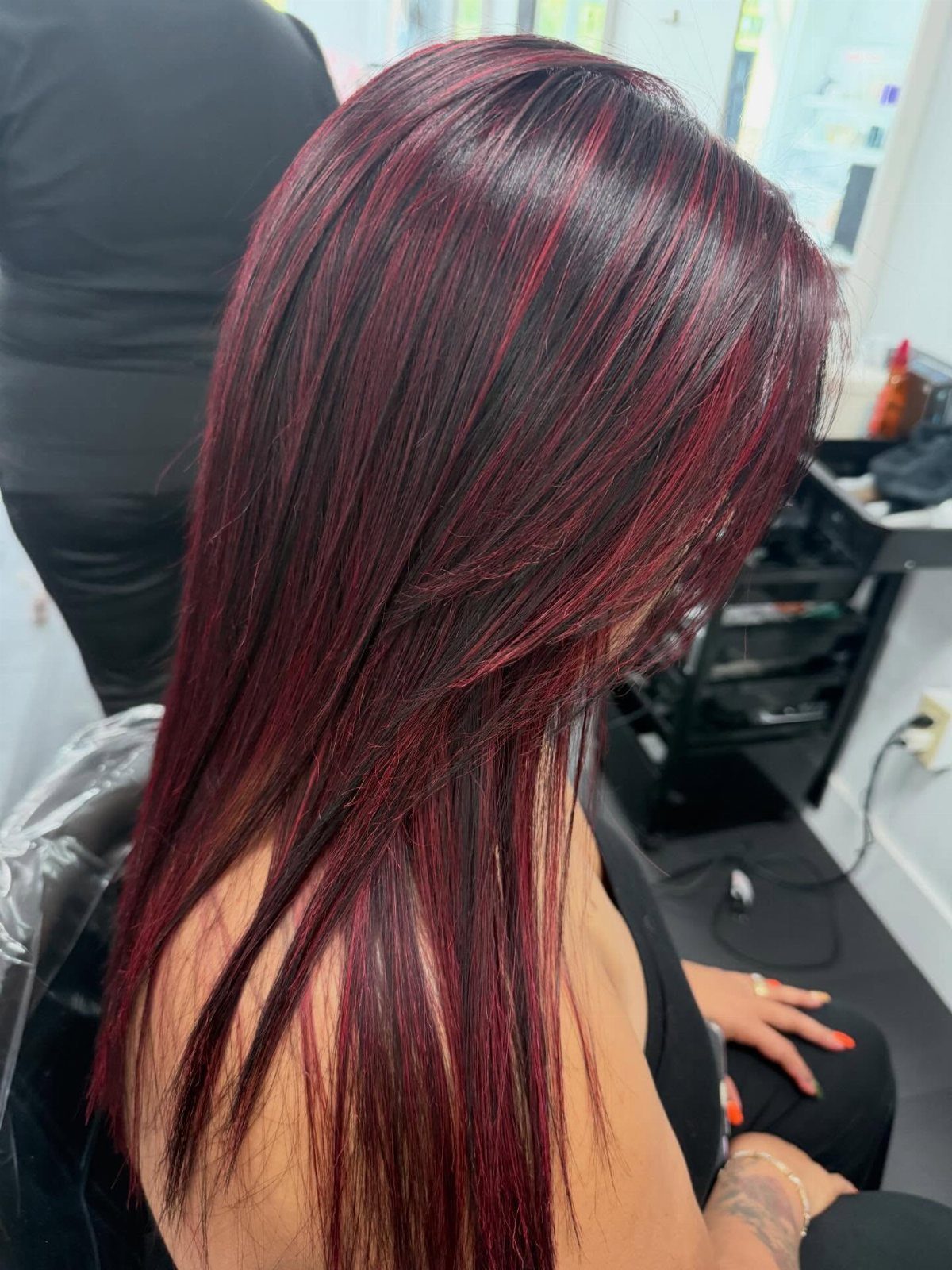 Long dark hair with burgundy-red streaks concentrated across the crown