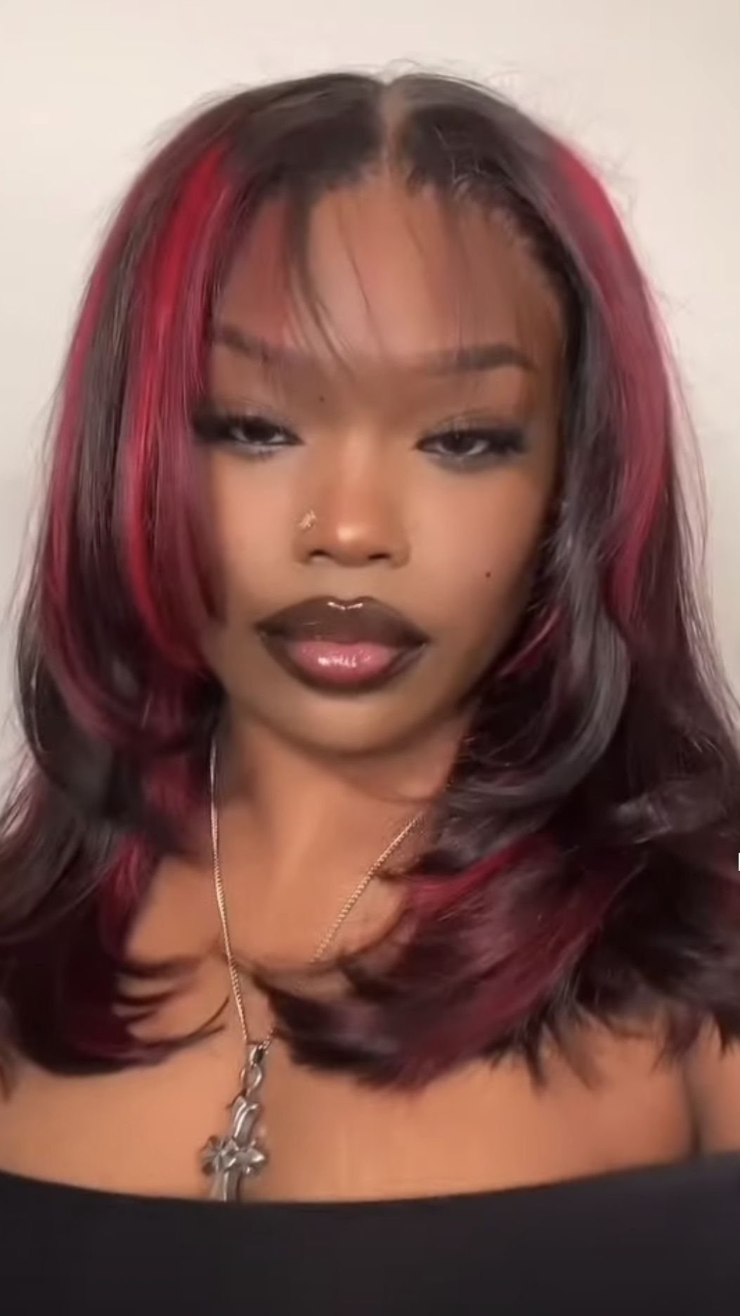 Woman with black layered hair, burgundy face-framing highlights, and wispy curtain bangs