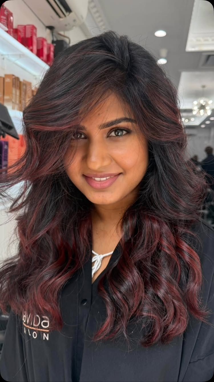 Woman with long black waves threaded with subtle burgundy-red highlights.
