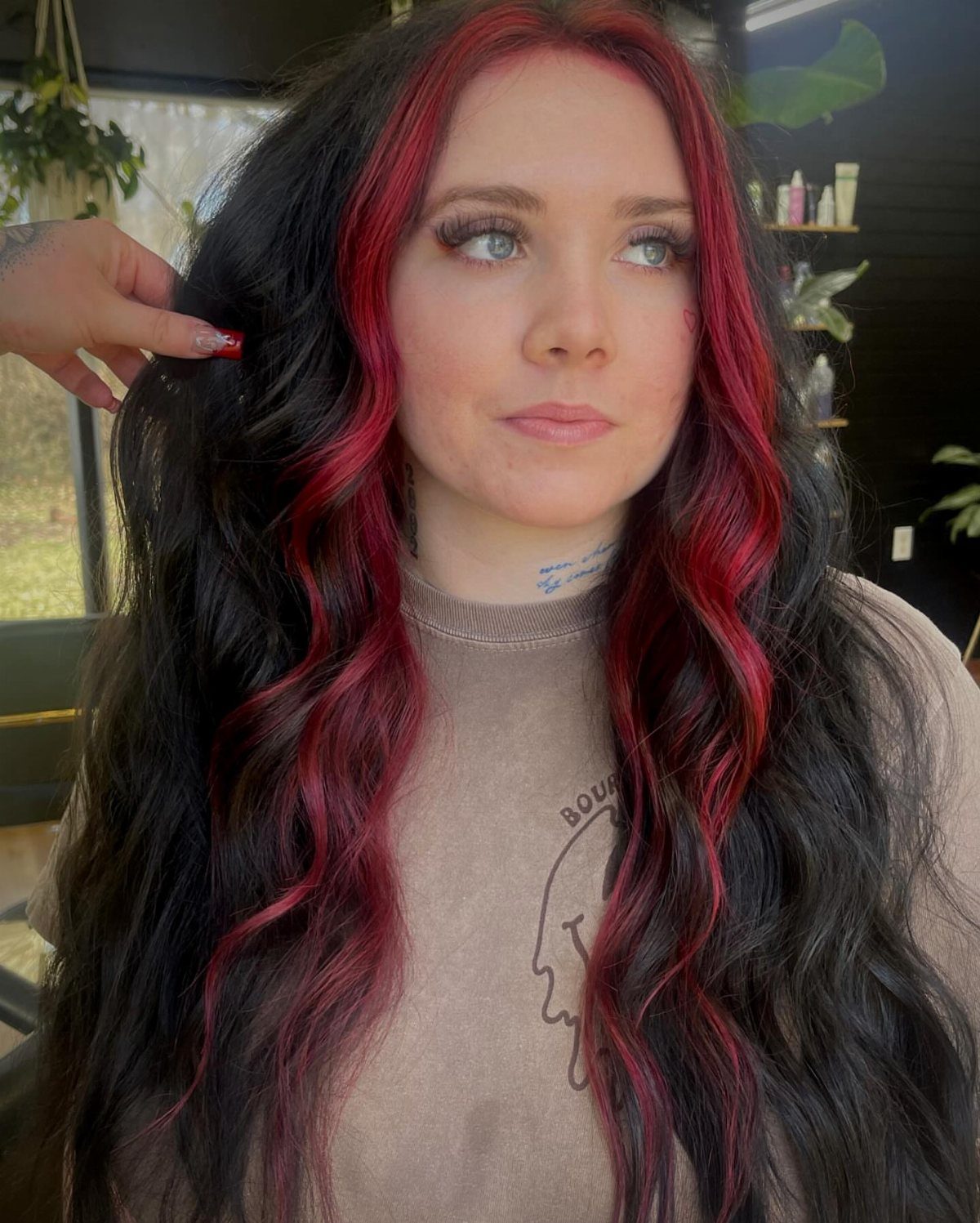 Woman with long black waves and vivid red face-framing streaks in a salon