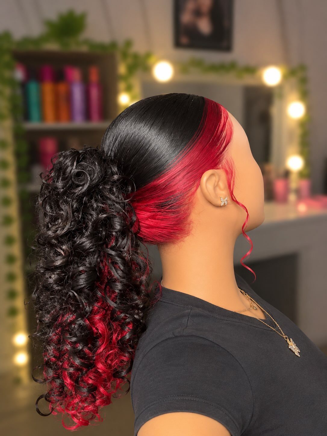 Black curly ponytail with vivid red streaks shown in a salon profile view
