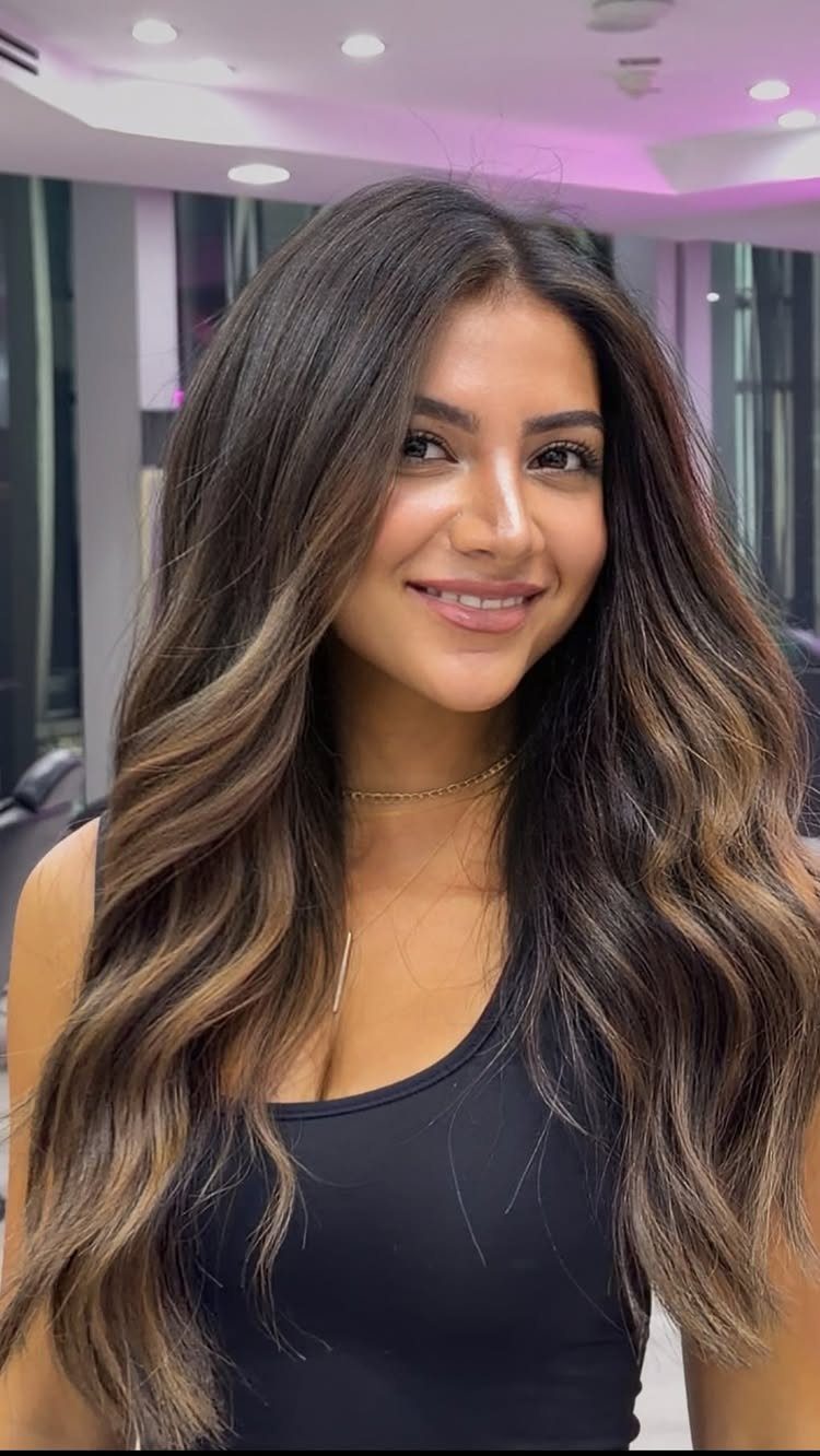 Woman displays long dark hair with warm caramel balayage highlights