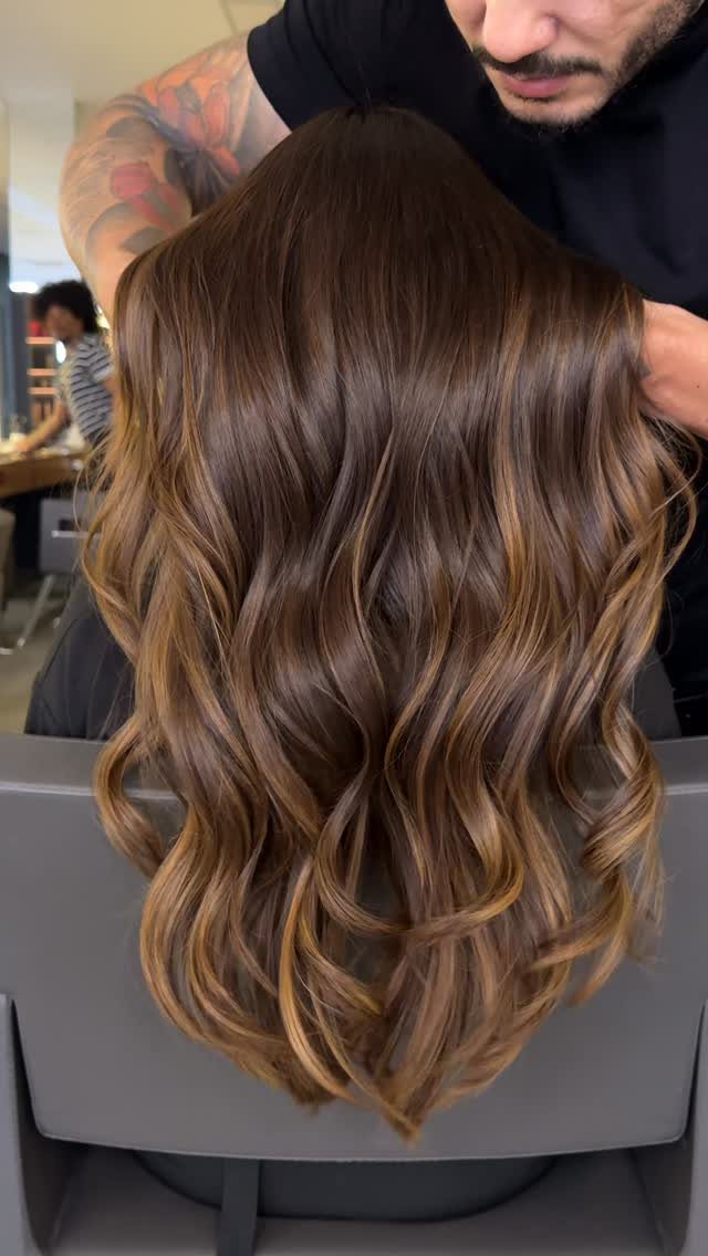 Long chocolate-brown balayage waves with lighter ribbons in a salon