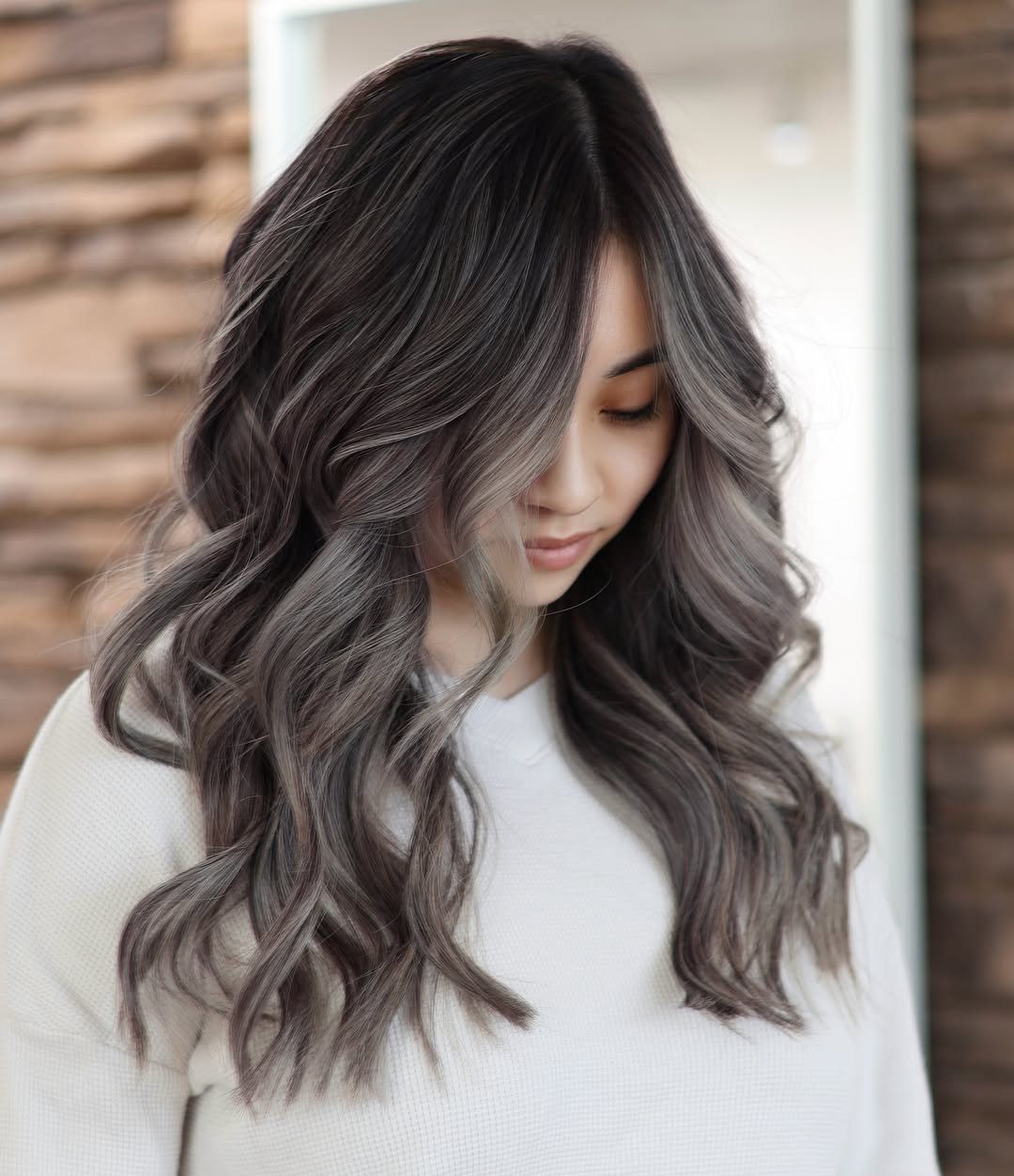 Woman showing long dark waves with smoky gray balayage highlights