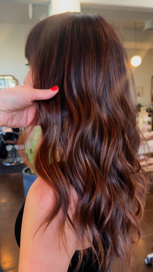 Long dark waves show subtle copper balayage as a hand touches the hair
