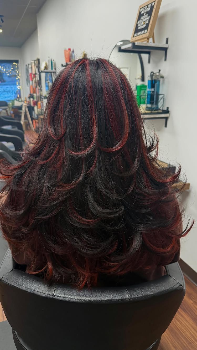 Long dark layered hair with vivid crimson-red balayage curls in a salon