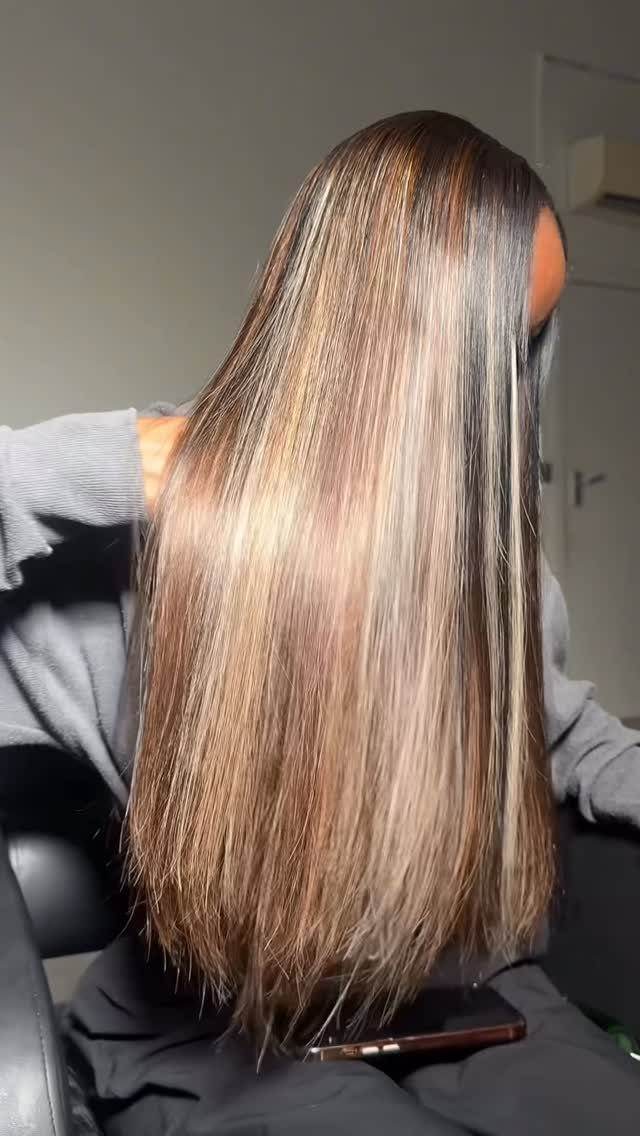 Long dark hair with warm honey balayage highlights over a salon cape