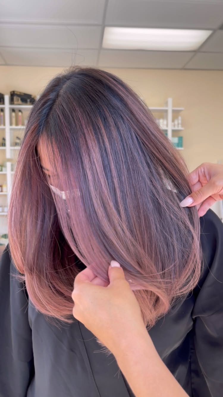 Long dark hair with rose-pink balayage highlights held apart in a salon