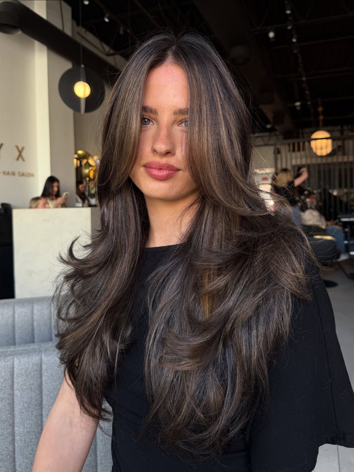 Woman with long dark hair showing subtle warm auburn balayage highlights