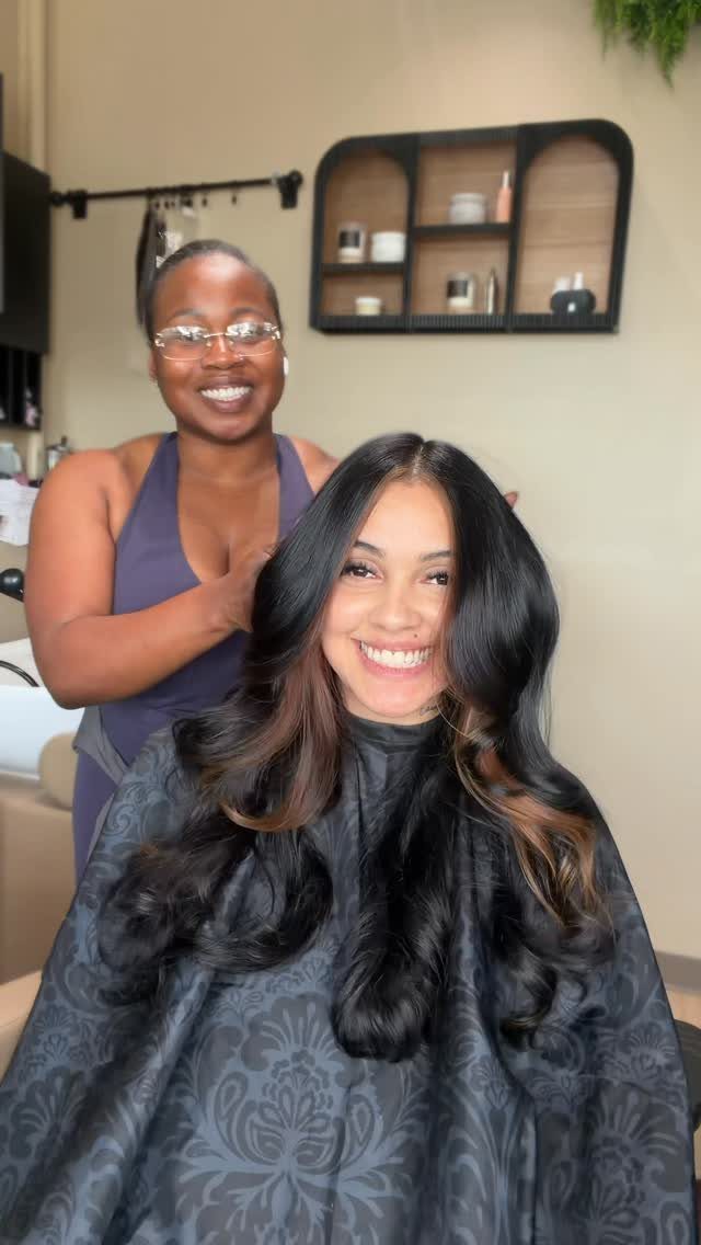 Woman with long black curls and subtle brown highlights seated in a salon