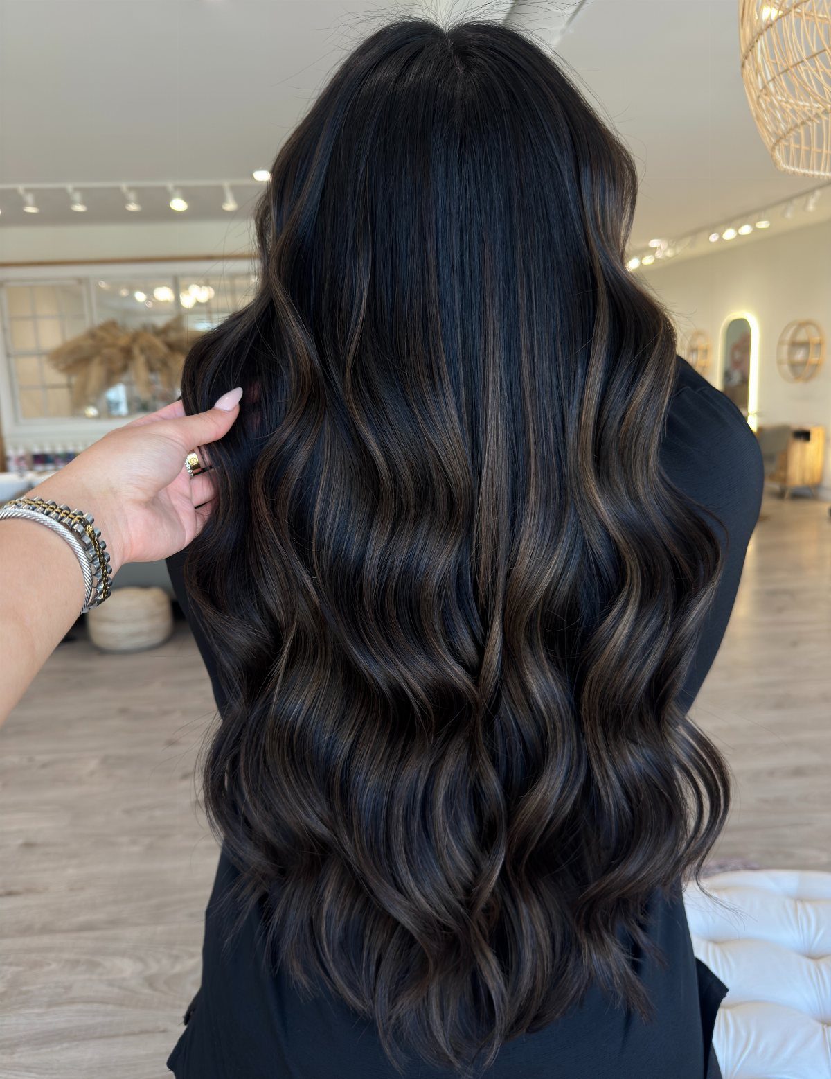 Long wavy black hair with prominent caramel brown streaks in a salon