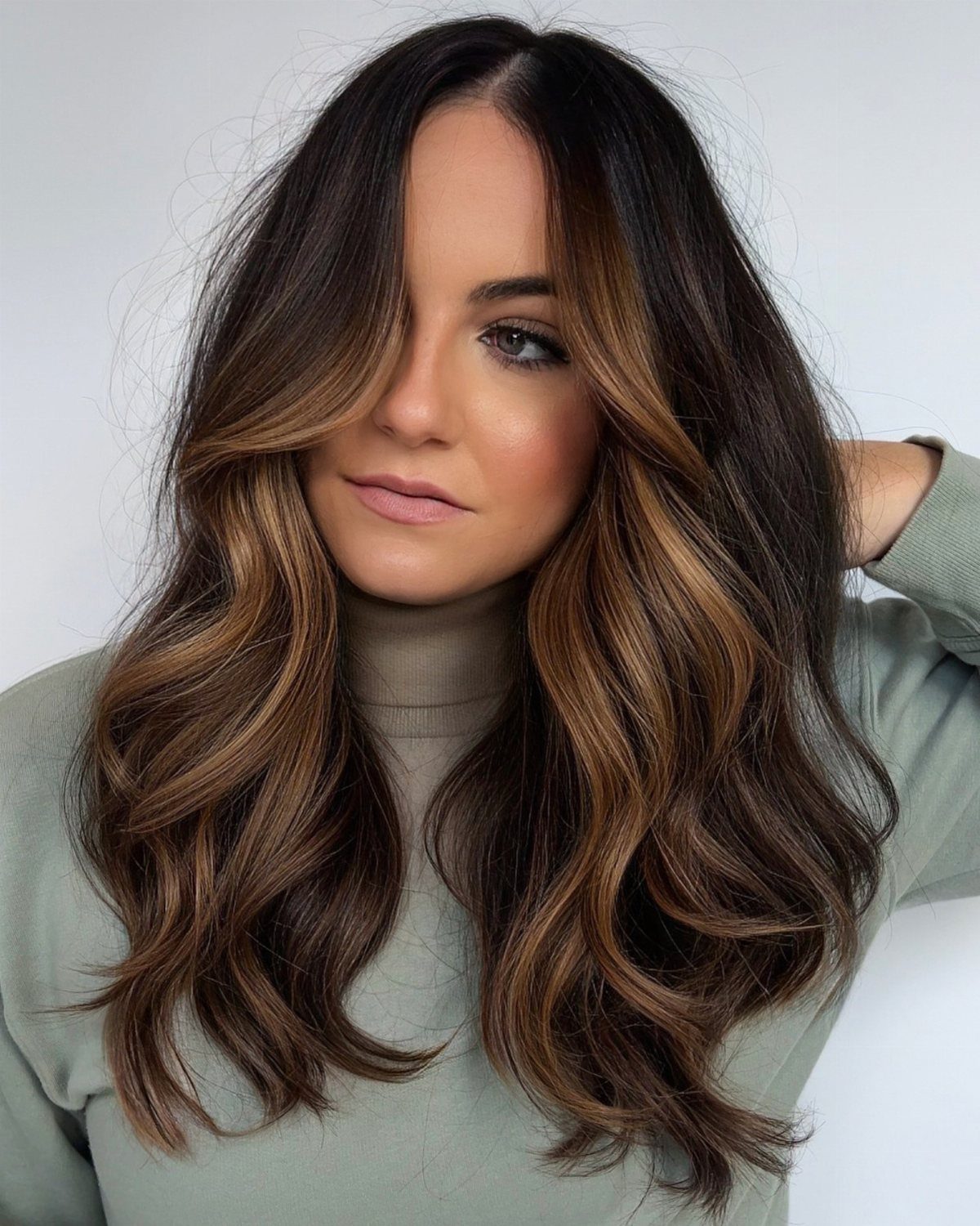 Woman with long dark waves and caramel face-framing highlights