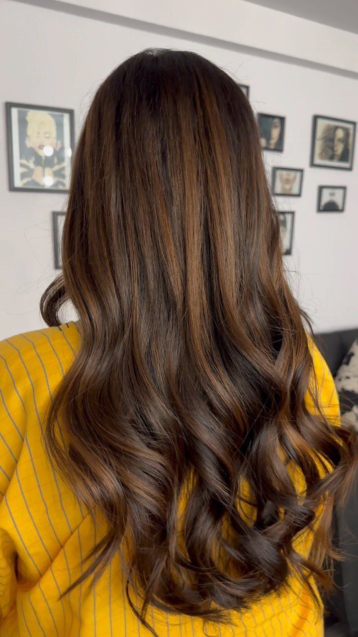 Long wavy dark hair with soft chocolate-brown highlights over a mustard striped top