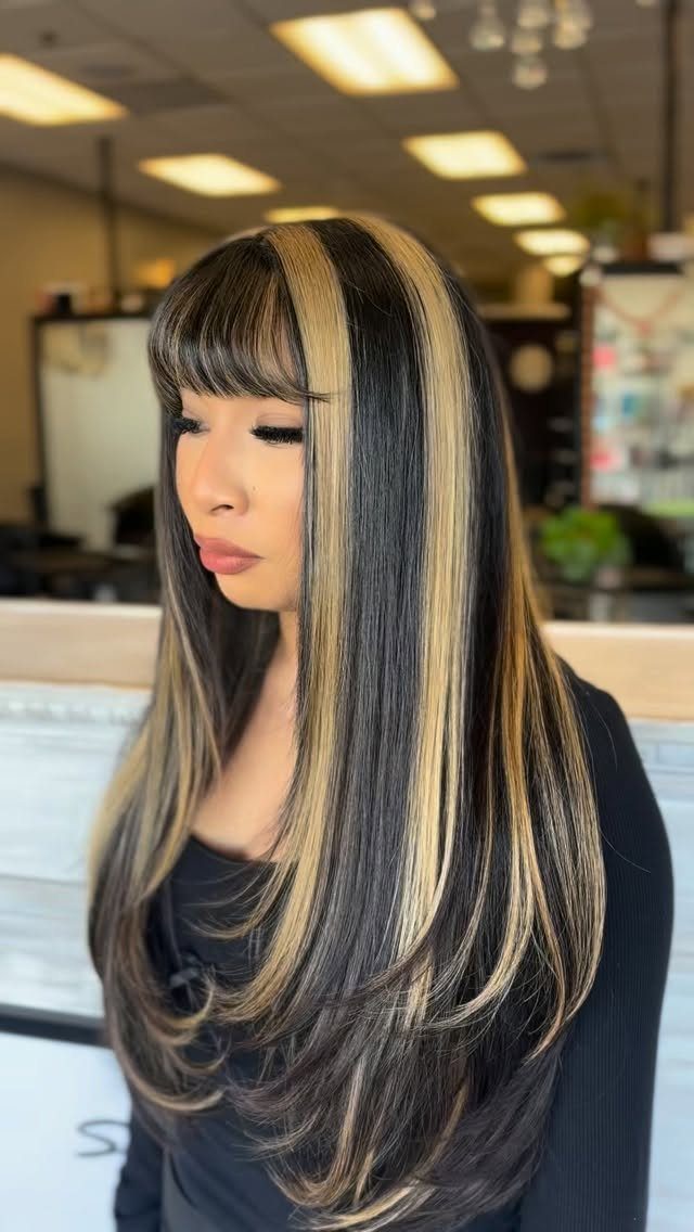 Woman with long black hair featuring wide contrasting brown and blonde highlights