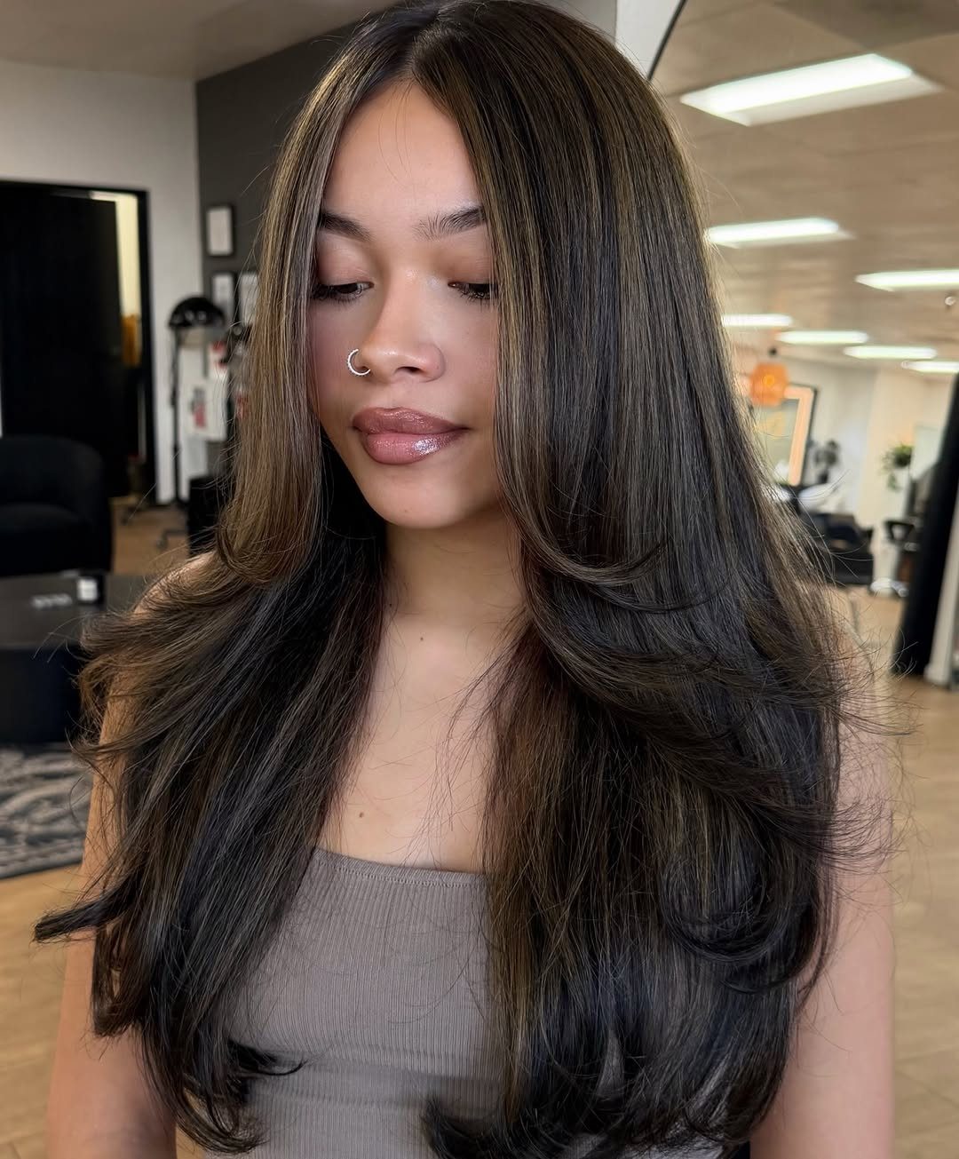 Woman with long layered black hair showing subtle dark brown highlights in a salon