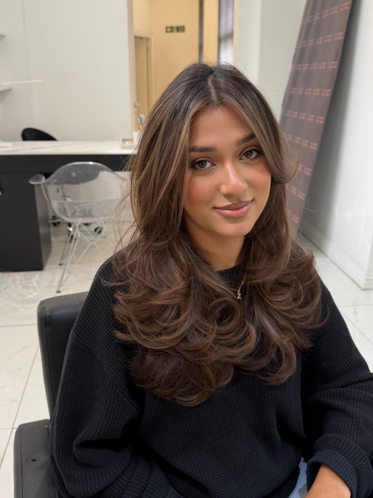 Woman with layered dark brown hair and warm face-framing highlights in a salon