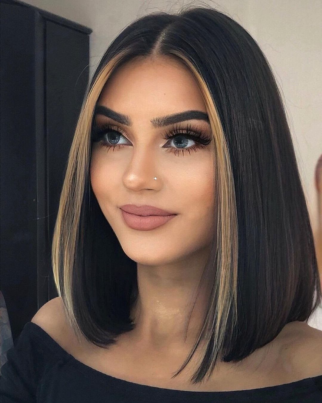 Woman showcasing black bob with golden brown face-framing money piece highlights