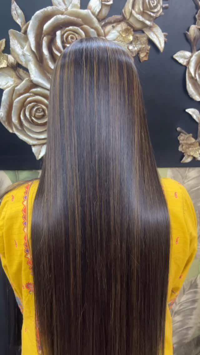 Long straight dark hair with subtle warm brown highlights against a floral wall