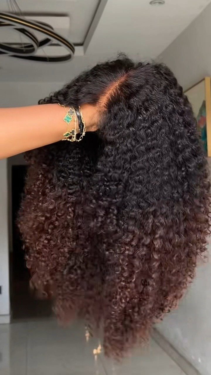 Curly black hair transitions into reddish-brown ends, held apart by a hand