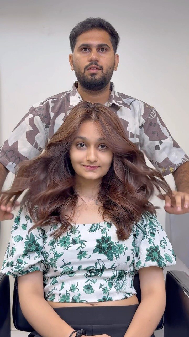 Woman with long wavy brown hair and warm caramel highlights seated in a salon