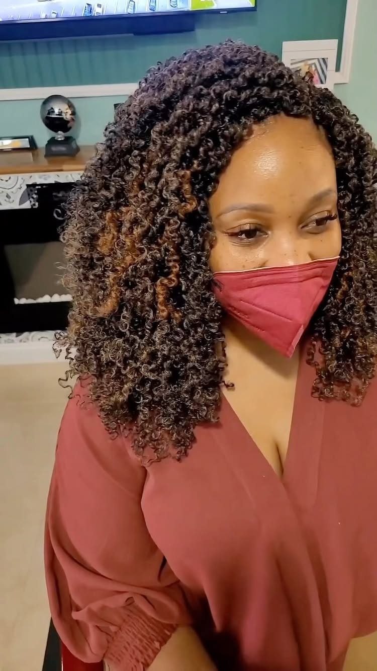 Dark curly hair with warm brown highlights frames a masked woman's face