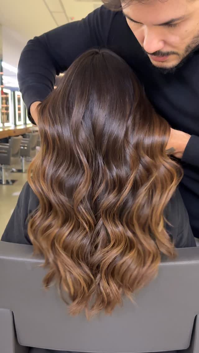 Long dark brown waves with subtle lighter chocolate-brown highlights in a salon