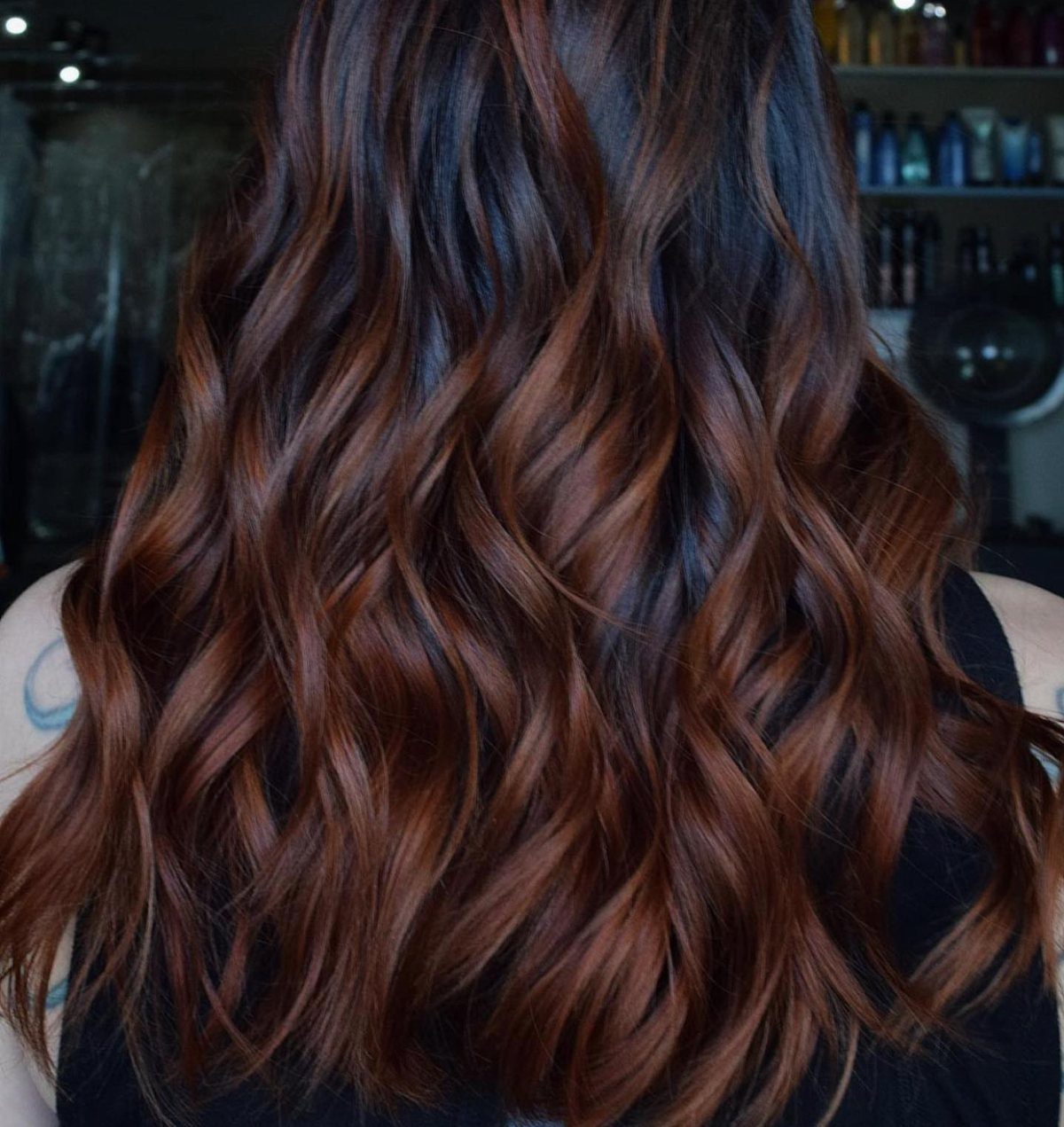 Wavy dark brown hair with copper-brown balayage highlights in a salon