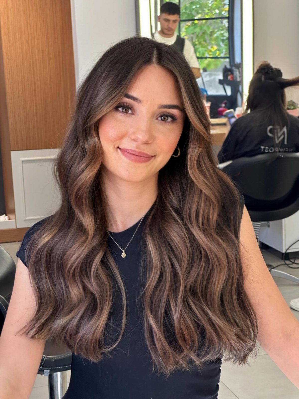 Woman showing long dark hair with soft hazelnut brown highlights in a salon